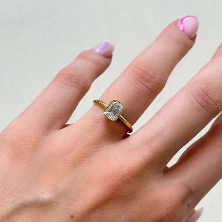 verlobungsring-bezel-moissanit-1ct-smaragdschliff-am-finger-gelbgold-stellar-hariets.jpg