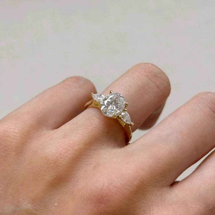 Verlobungsring-Trinity-Seraphina-Moissanit-2ct-ovalgeschliffener-Mittelstein-Seitenansicht-am-Finger-Gelbgold-Hariets.jpg